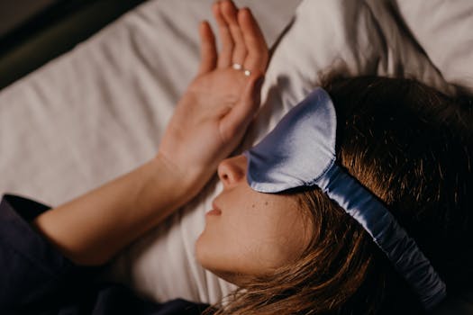 A woman peacefully sleeping in bed, wearing a blue silk eye mask for comfort and relaxation.